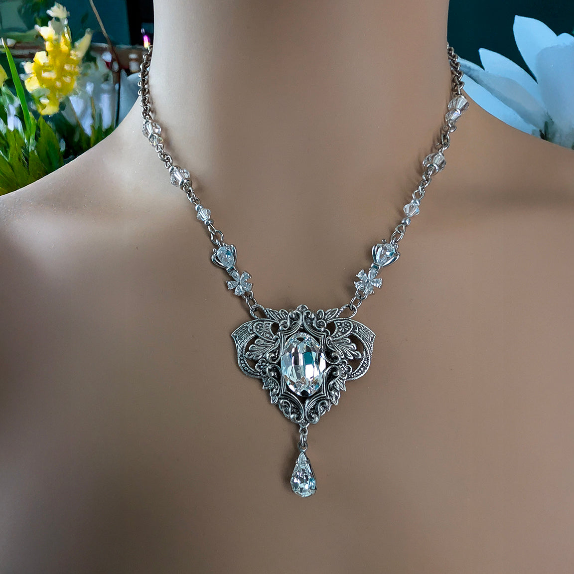 An ornate silver vintage-style bridal necklace displayed on a model bust, featuring a clear Swarovski crystal pendant and smaller clear crystal details along the chain.