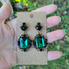 Vintage emerald green crystal earrings displayed upon a piece of cardstock with a natural background.
