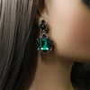 Vintage emerald green crystal earrings displayed on a mannequin ear.