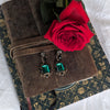 Vintage emerald green crystal earrings displayed on a brown suede book with a red rose. 
