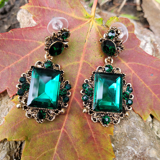 Vintage emerald green crystal earrings displayed on a red leaf.
