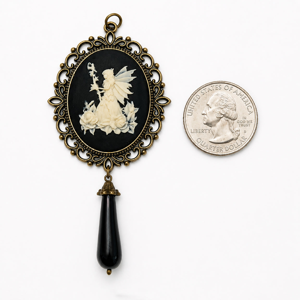 Decorative cameo pendant with fairy design next to a quarter for scale on a white background