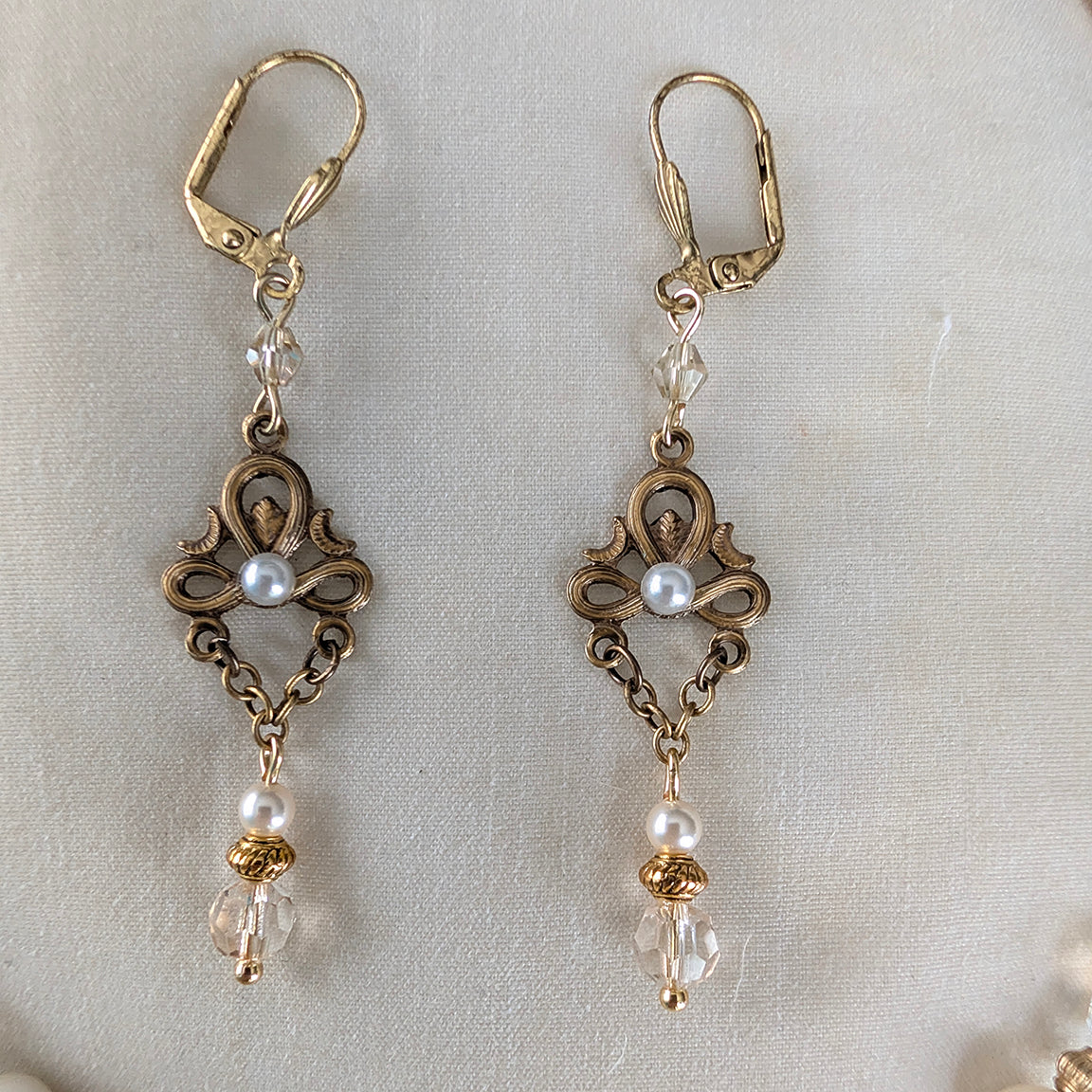 Pair vintage styled of gold and pearl crystal earrings on a light fabric background