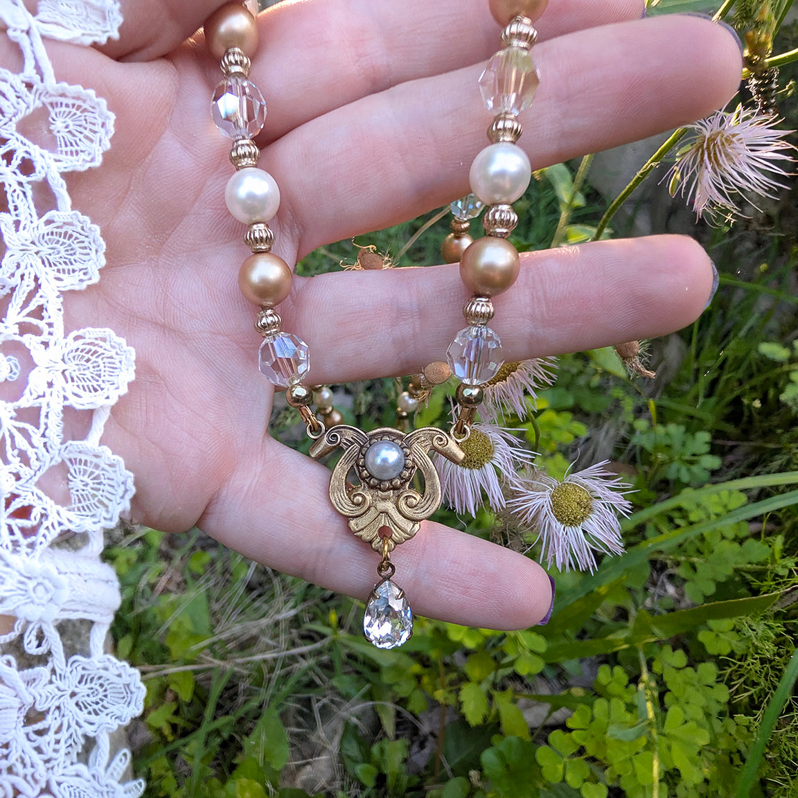 Hand holding a Vintage bridal Swarovski Crystal, Ivory and Gold Pearl necklace against a natural background