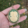 Gold and green cameo locket pendant held in a hand with a grassy backgroundb
