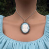 Necklace with a cameo locket pendant on a model wearing a light blue dress.