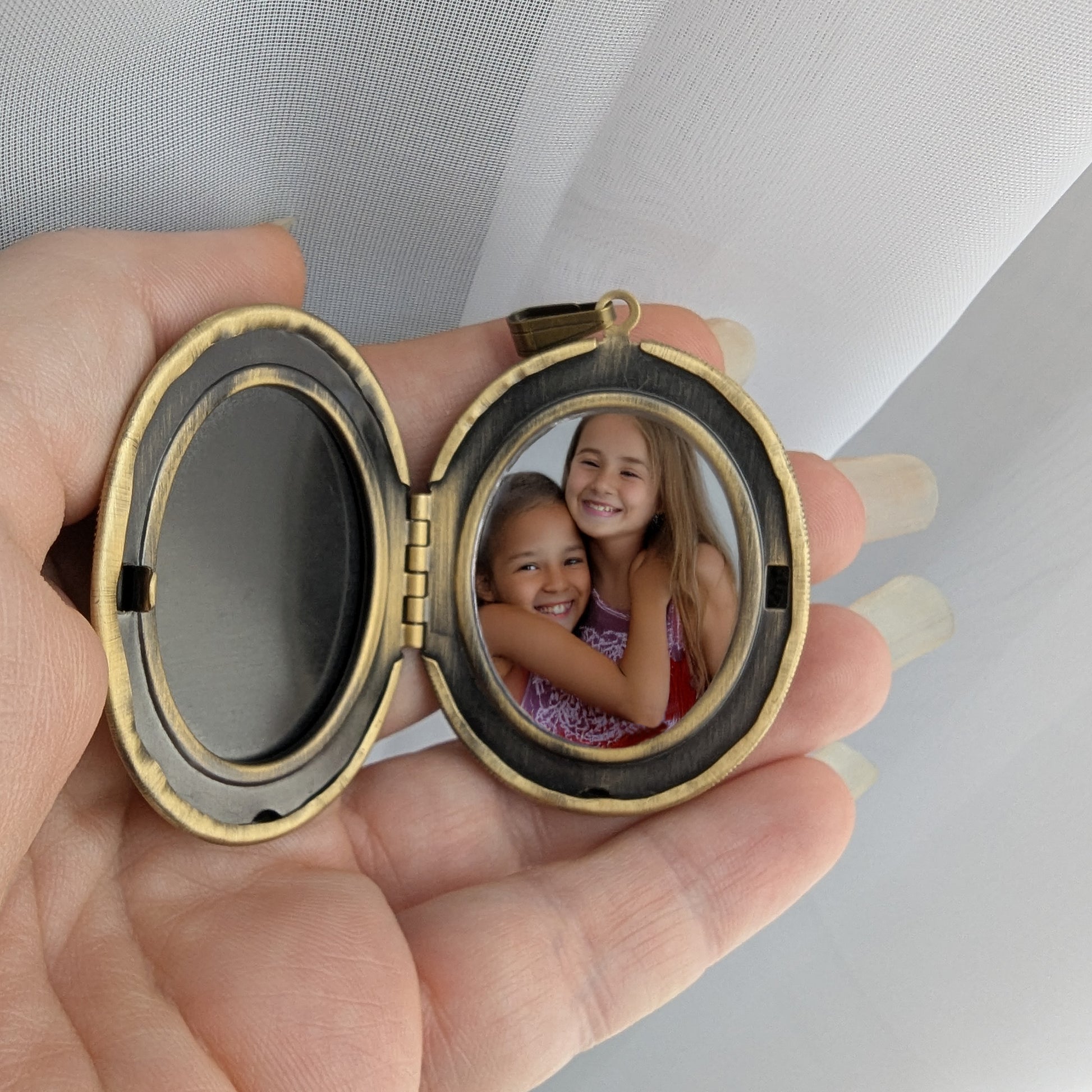 Hand holding a round locket with two smiling girls inside, against a neutral background.